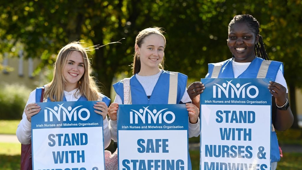 Two female nurses in scrubs standing outside the Oncology Unit smiling 